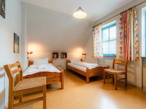 A room with two wooden beds, a wooden chair, a small table, and a window with curtains. - OG in the Reimer House (St. Peter-Ording)
