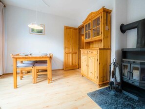 A wooden dining table with chairs, a cabinet with glass doors, a fireplace, and a hanging light fixture. - OG in the Reimer House (St. Peter-Ording)