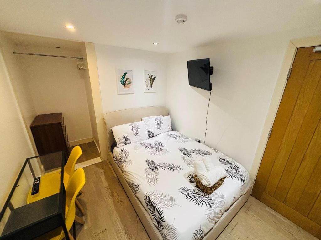 A bedroom with a bed, a desk with a chair, a television, and a door.