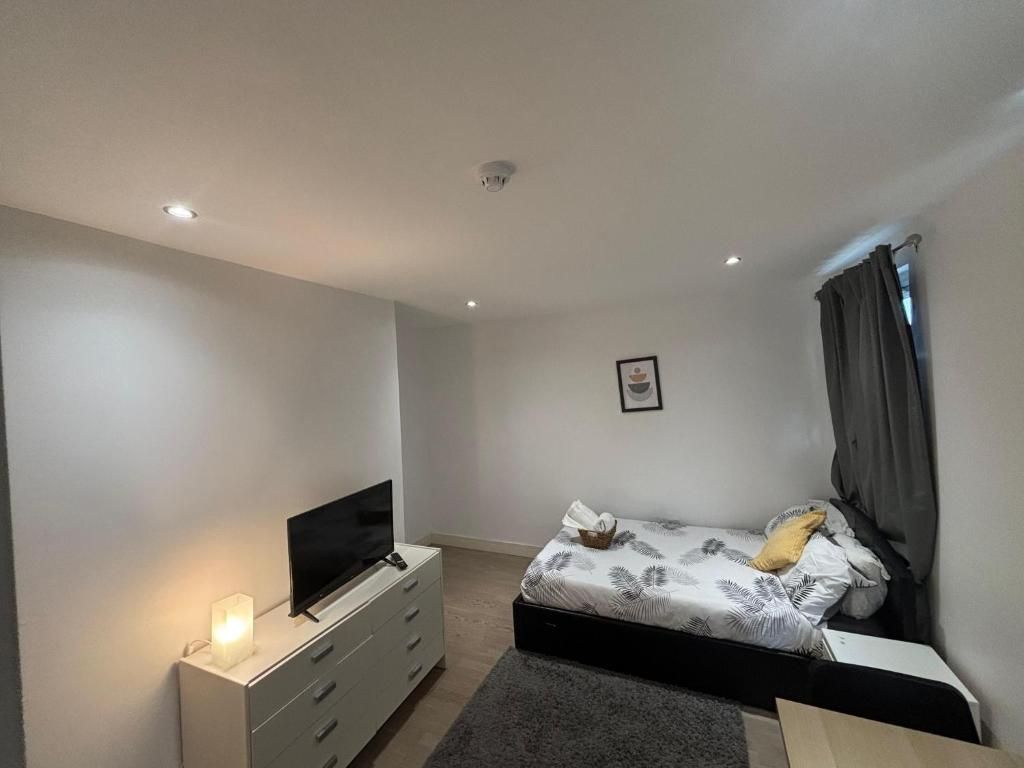 Un dormitorio con una cama, un televisor sobre un soporte, una mesita de noche e imagen colgada en la pared.