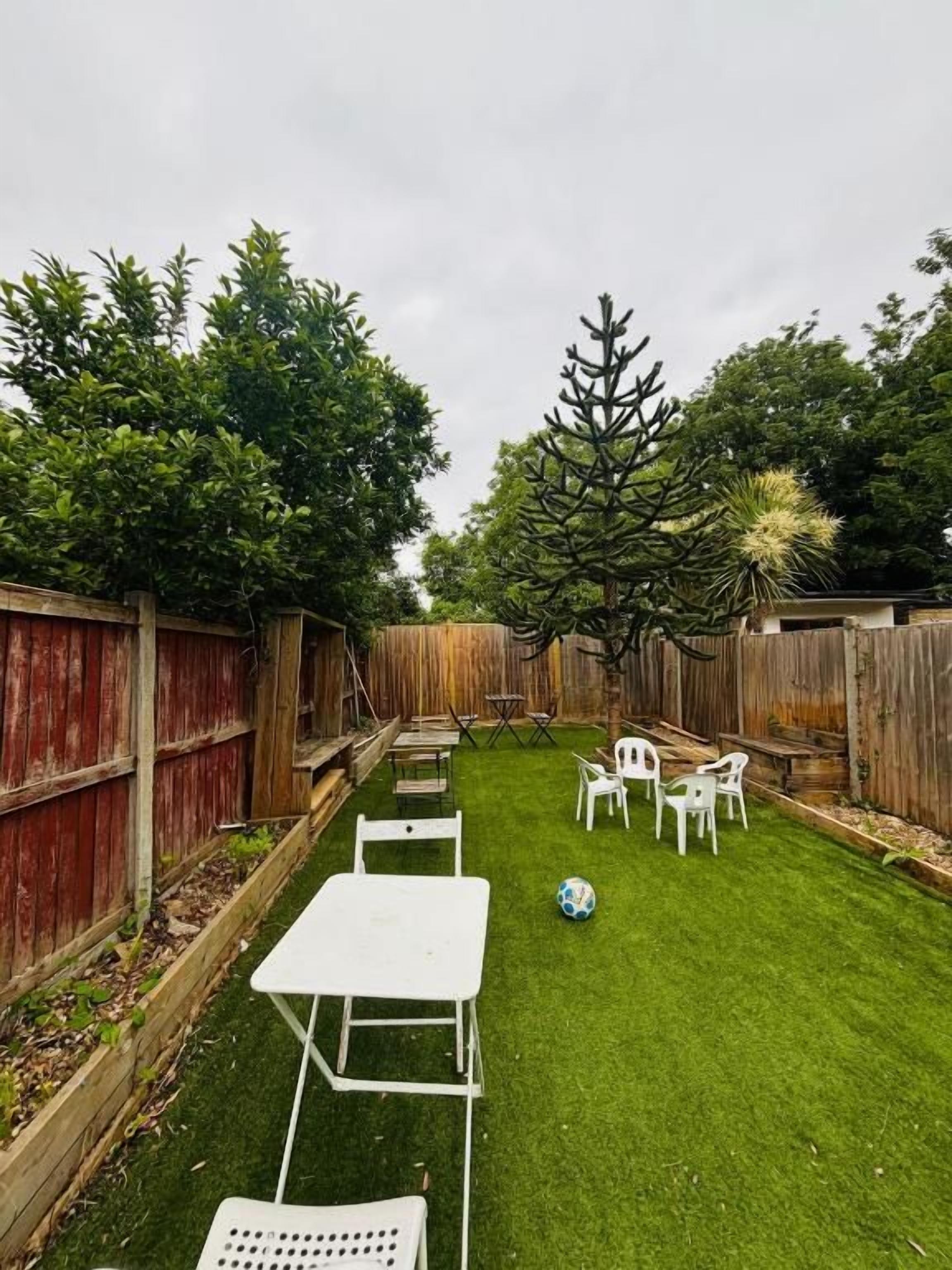 A backyard with a grassy lawn, white tables, and chairs, surrounded by wooden fences and trees.