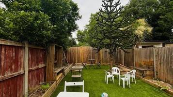 A backyard with a grassy lawn, white tables, and chairs, surrounded by wooden fences and trees.