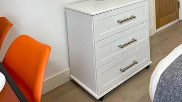 Une pièce dotée d’un téléviseur à écran plat fixé au mur, d’une commode blanche avec des tiroirs et d’une porte en bois.