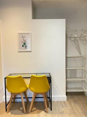 A room with a white wall, a framed picture, a black desk with two yellow chairs, and a white shelving unit.