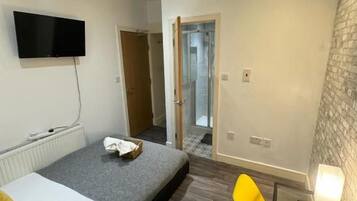 Una habitación con una cama, un televisor de pantalla plana en la pared, una silla y una mesita con una lámpara.