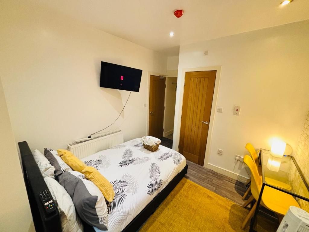 A bedroom with a bed, a TV mounted on the wall, a wooden door, and a small table with chairs.