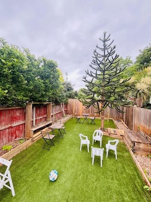 A backyard with a small lawn, white plastic chairs, and a wooden fence.