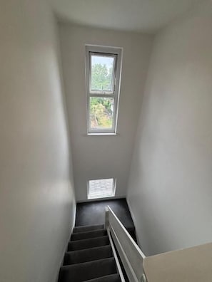 Una escalera estrecha con una ventana en la parte superior, que lleva a un rellano.