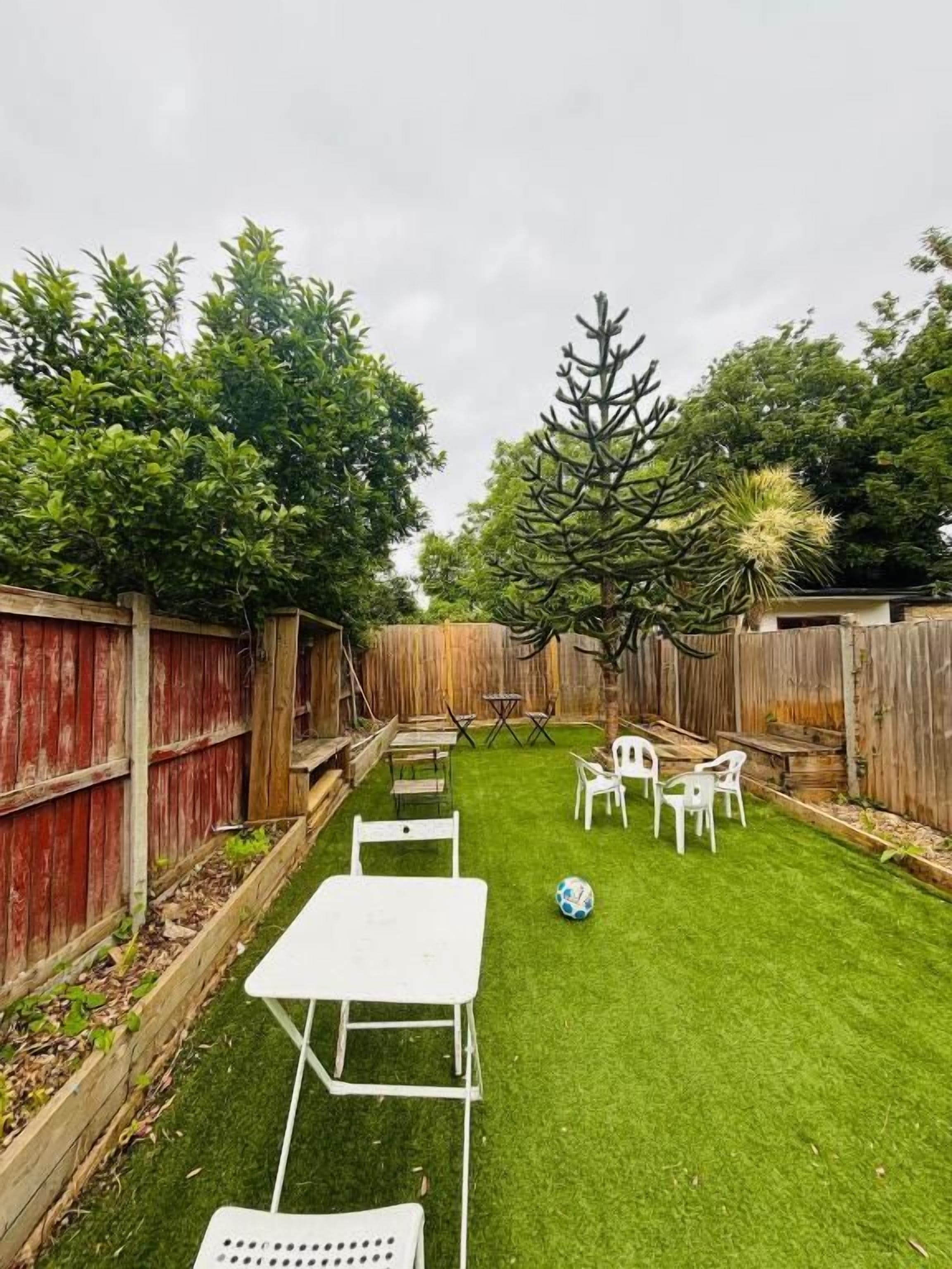 Un jardin avec une table et des chaises blanches, un ballon de foot et un arbre.