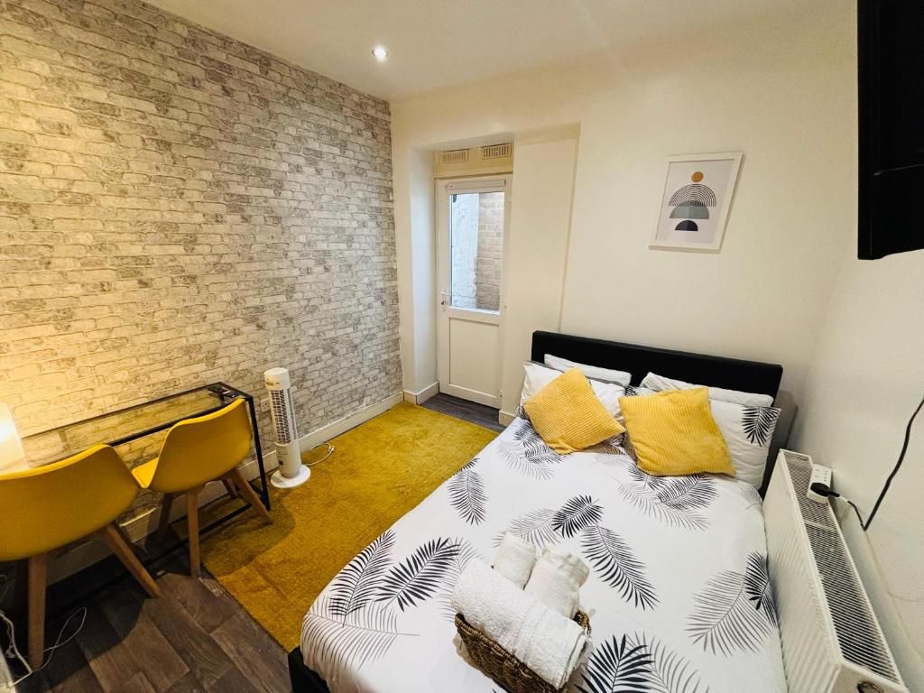 Une chambre d’hôtel avec un mur en briques, un lit recouvert d’une courtepointe à motifs de feuilles, un bureau avec des chaises et un radiateur.