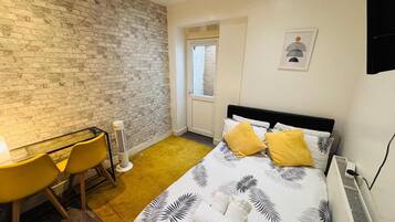 Une chambre d’hôtel avec un mur en briques, un lit recouvert d’une courtepointe à motifs de feuilles, un bureau avec des chaises et un radiateur.