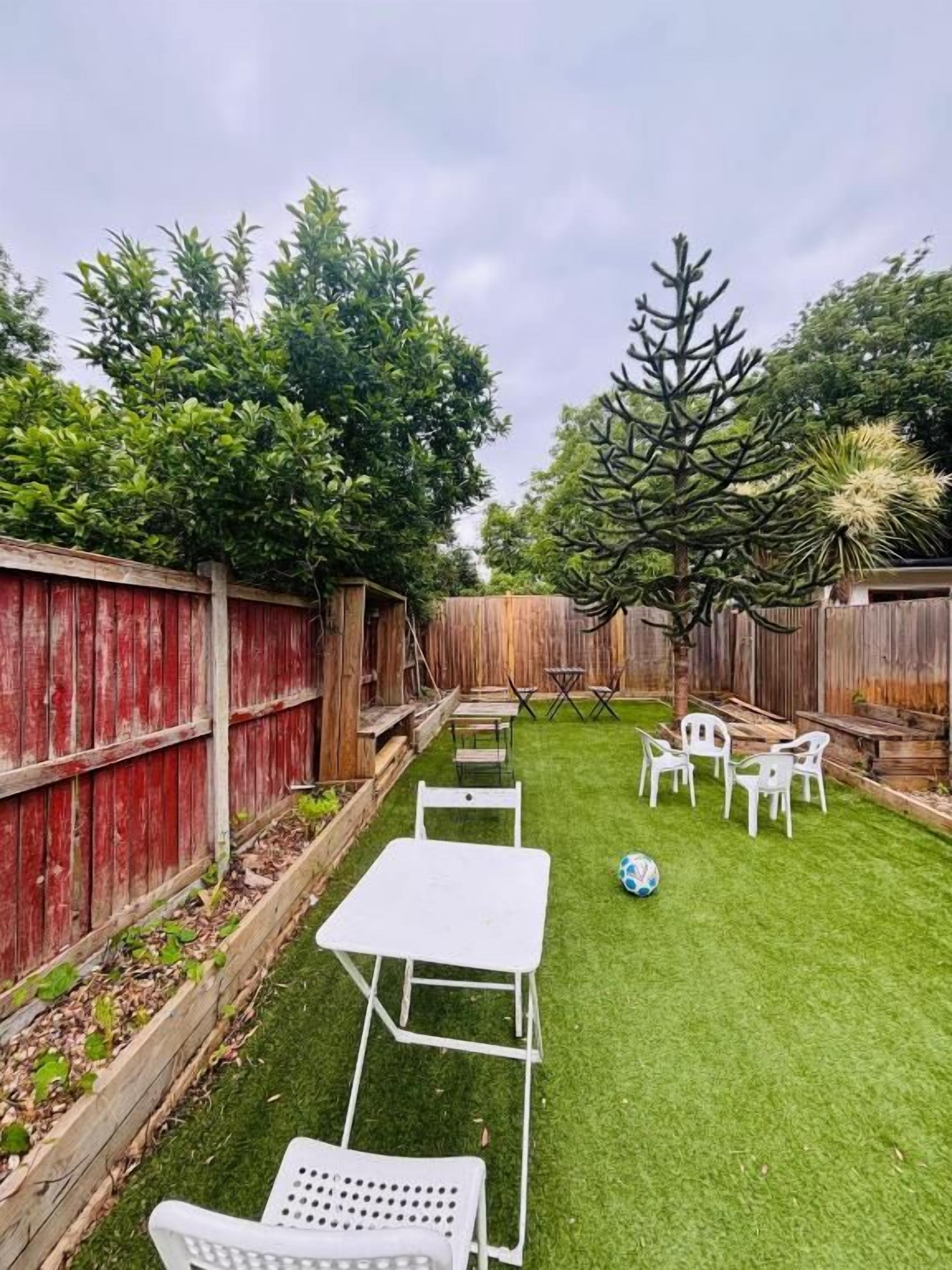 Un jardin avec une clôture en bois, une petite pelouse et des meubles d’extérieur blancs.