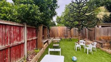 A backyard with a wooden fence, a small lawn, and white outdoor furniture.