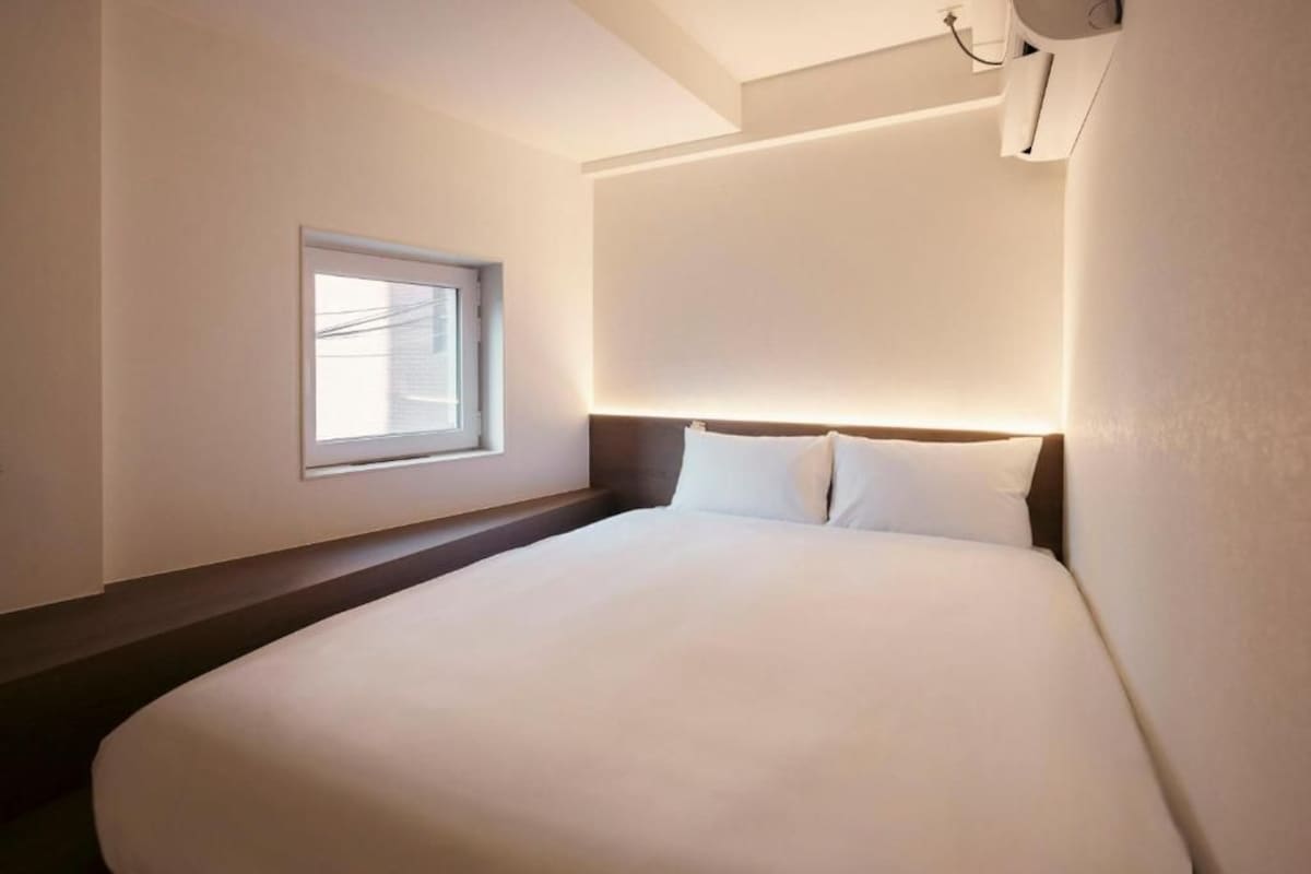 Quarto de hotel com uma cama grande, uma janela e um ar condicionado fixado na parede.