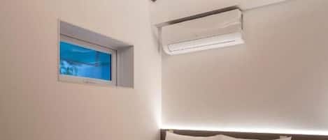 A hotel room with a bed, a window, and an air conditioning unit.