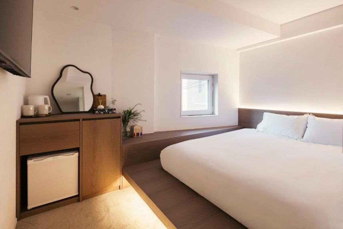 Quarto moderno com cama grande, mesa de cabeceira, espelho e um pequeno armário.