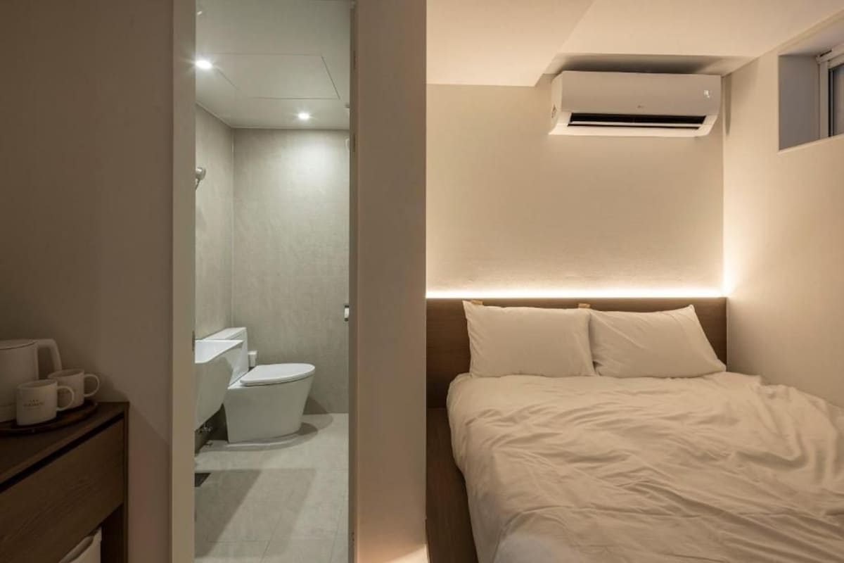 Quarto de hotel com cama, mesa de cabeceira e ar condicionado fixado na parede.