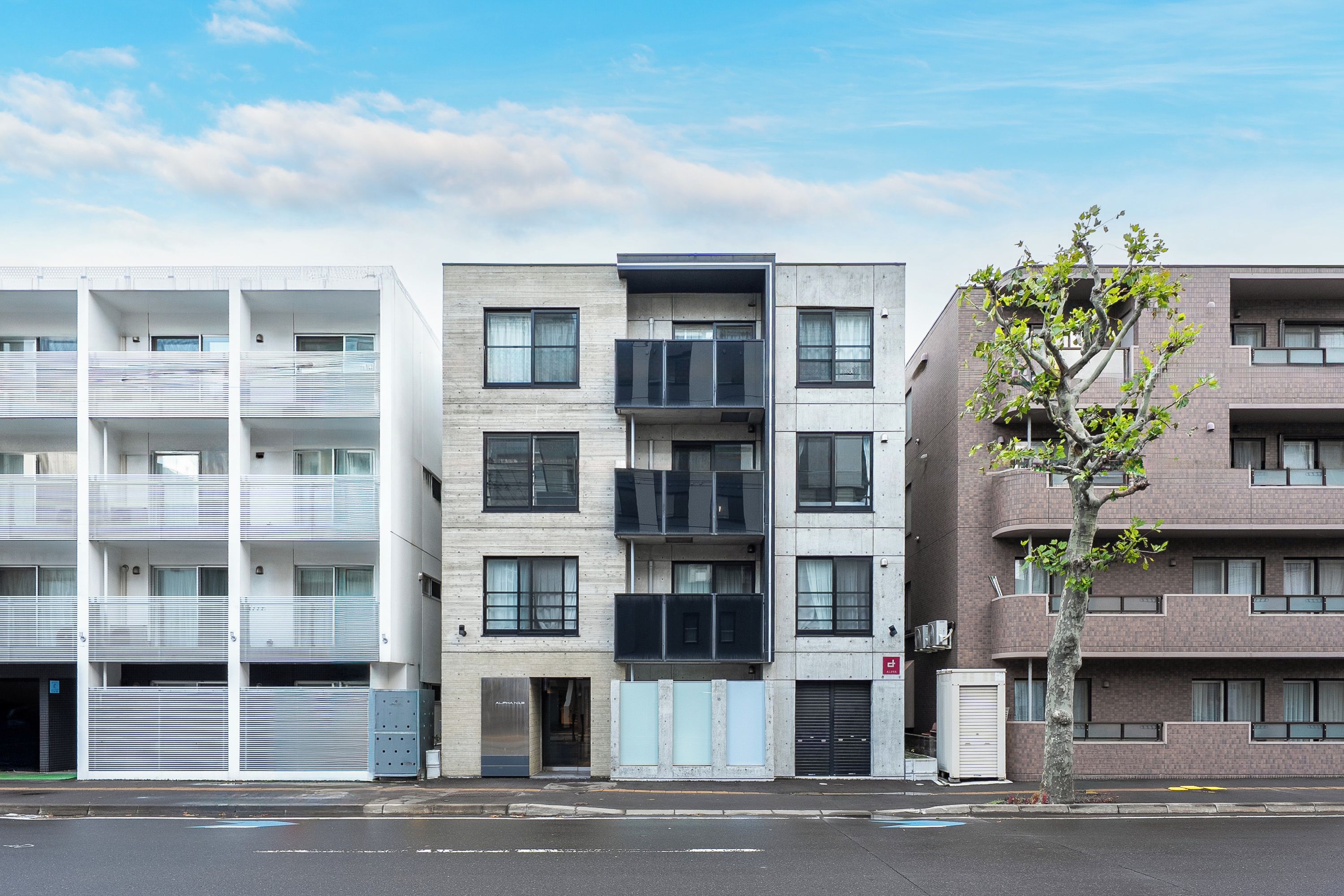 A multi-story building with balconies, a tree in front, and a clear sky.