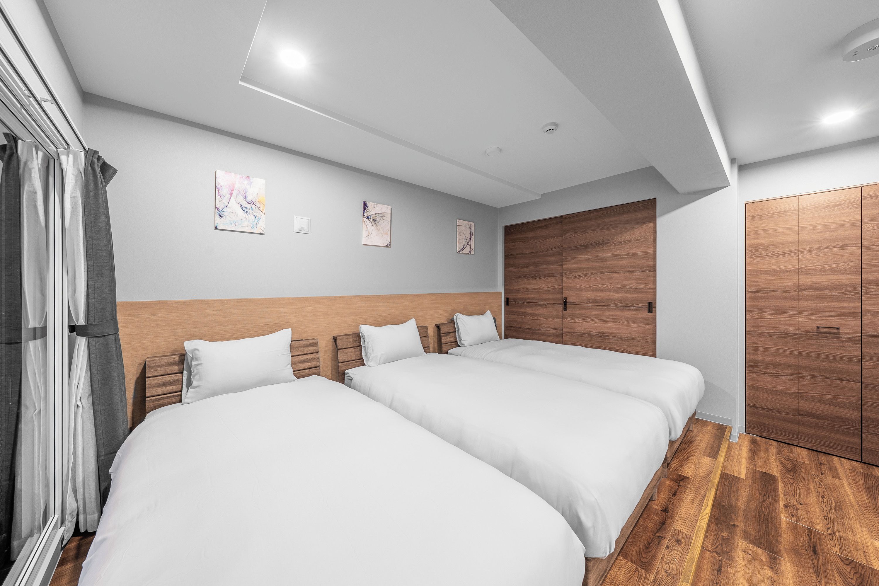 A hotel room with two beds, wooden headboards, a wooden wardrobe, and a ceiling light.