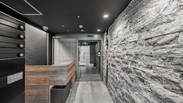 A modern reception area with a stone wall, a wooden reception desk, and a glass door leading to a hallway.