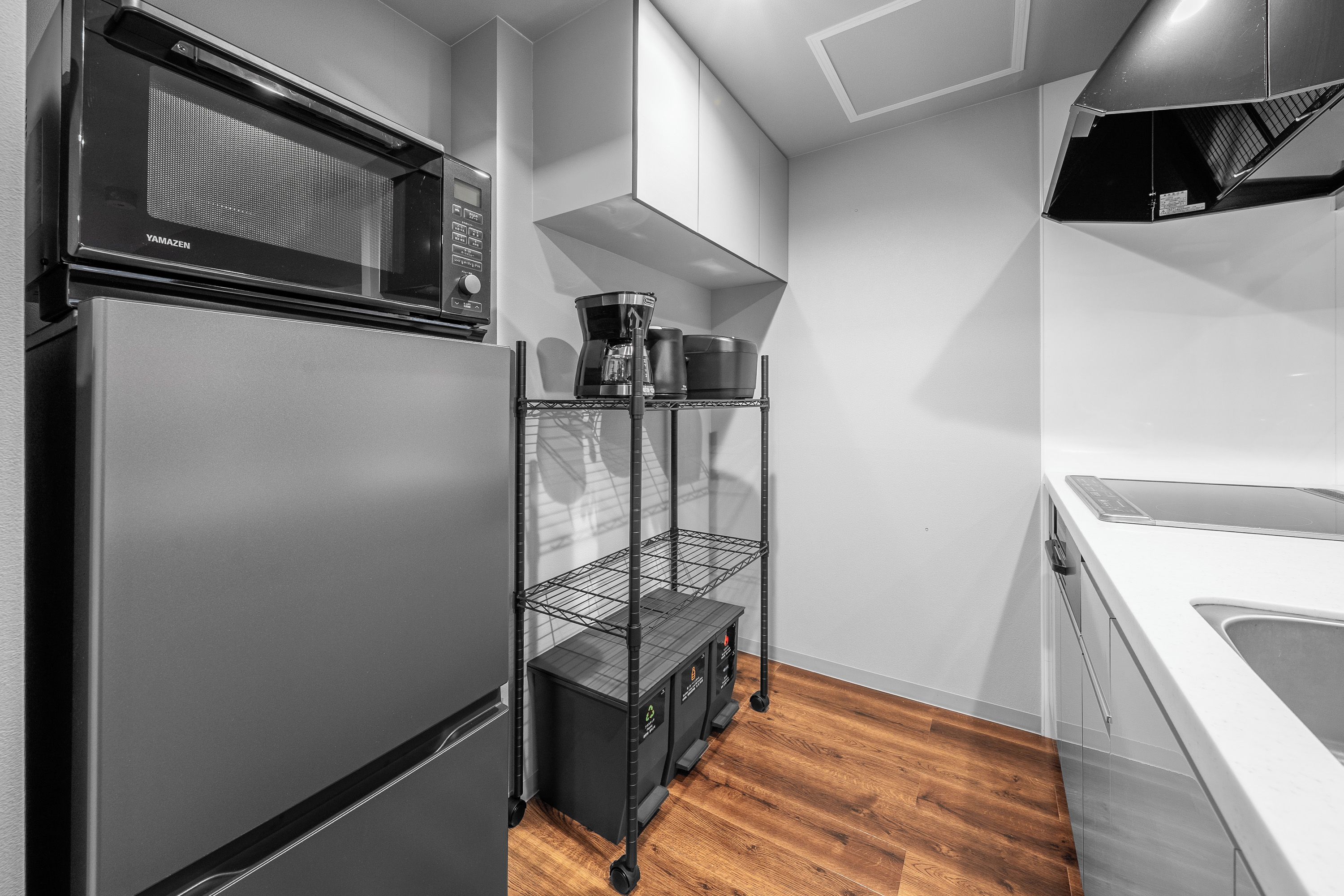 A modern kitchen with a stainless steel refrigerator, a microwave, a coffee maker, and a black storage unit with wheels.