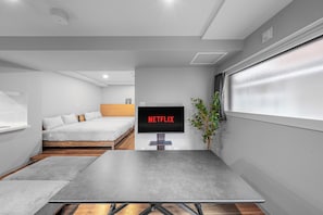 A modern bedroom with a bed, a TV mounted on the wall, and a window with curtains. - NOBLE 202 (Sapporo)