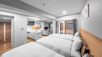 A modern hotel room with two beds, a kitchenette, a bathroom, and a view of the outdoors.