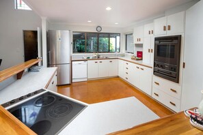 Uma cozinha moderna com armários brancos, geladeira de aço inoxidável, forno embutido e uma janela que traz luz natural.