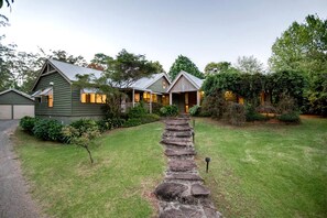 A two-story house with a stone pathway leading to the entrance, surrounded by a well-maintained lawn and various shrubs. - Gorgeous Country Cottage with a Fireplace near D'aguilar National Park, Queensland (Mount Glorious)
