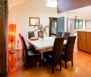 A dining area with a table and chairs, a vase with flowers, and a kitchen in the background. - Gorgeous Country Cottage with a Fireplace near D'aguilar National Park, Queensland (Mount Glorious)