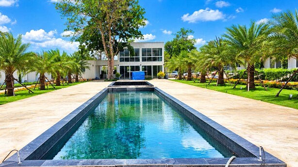 A rectangular pool with a clear blue water surface, surrounded by a paved walkway and palm trees. - Mangrove Resort Phuket Airport (Thalang)
