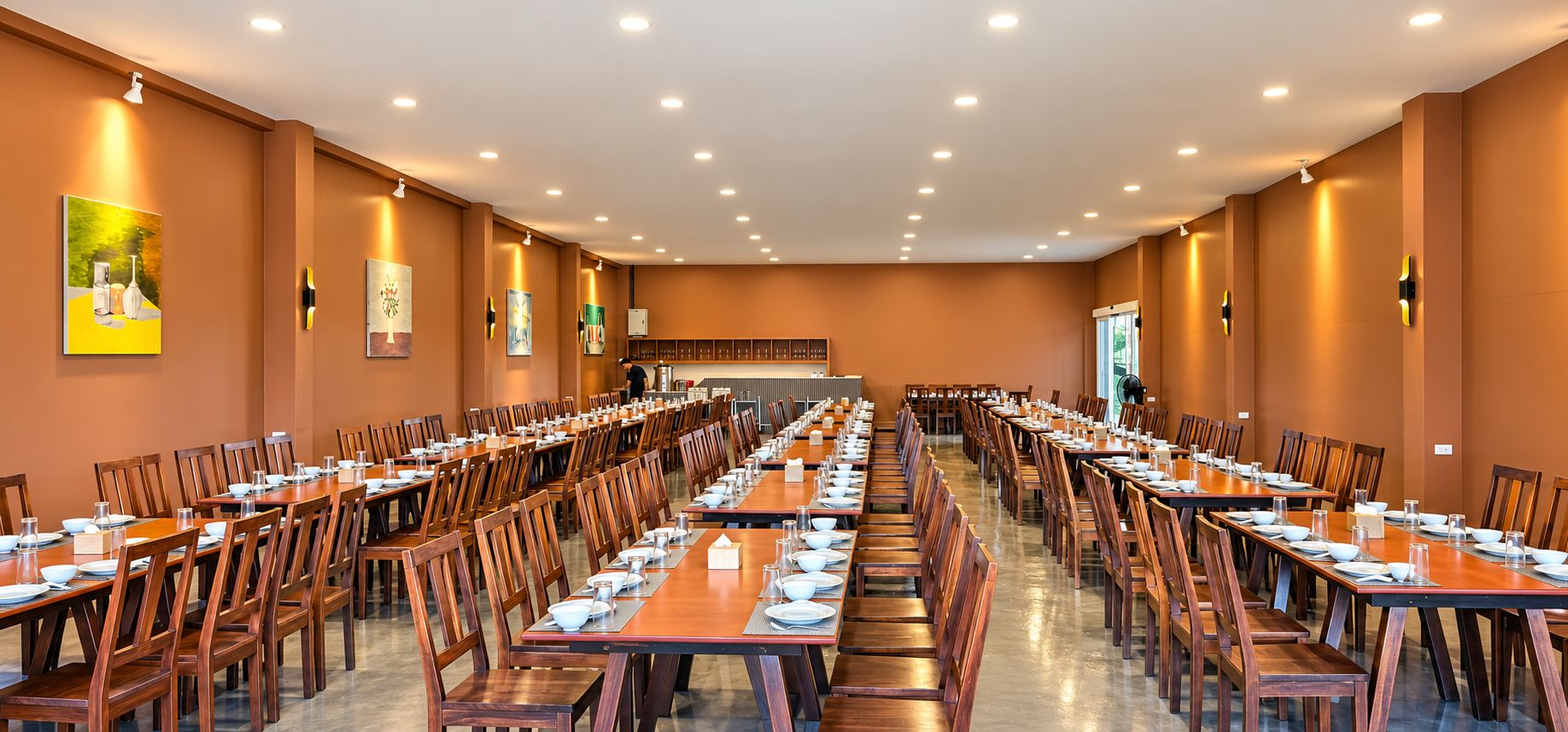 A large dining hall with multiple tables and chairs, arranged in rows.
