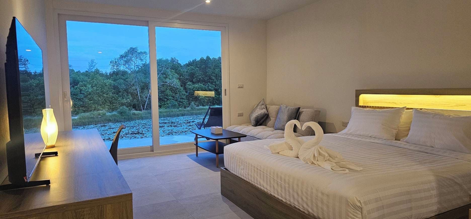 A hotel room with a bed, a desk, a chair, and a view of a natural landscape through a sliding door.