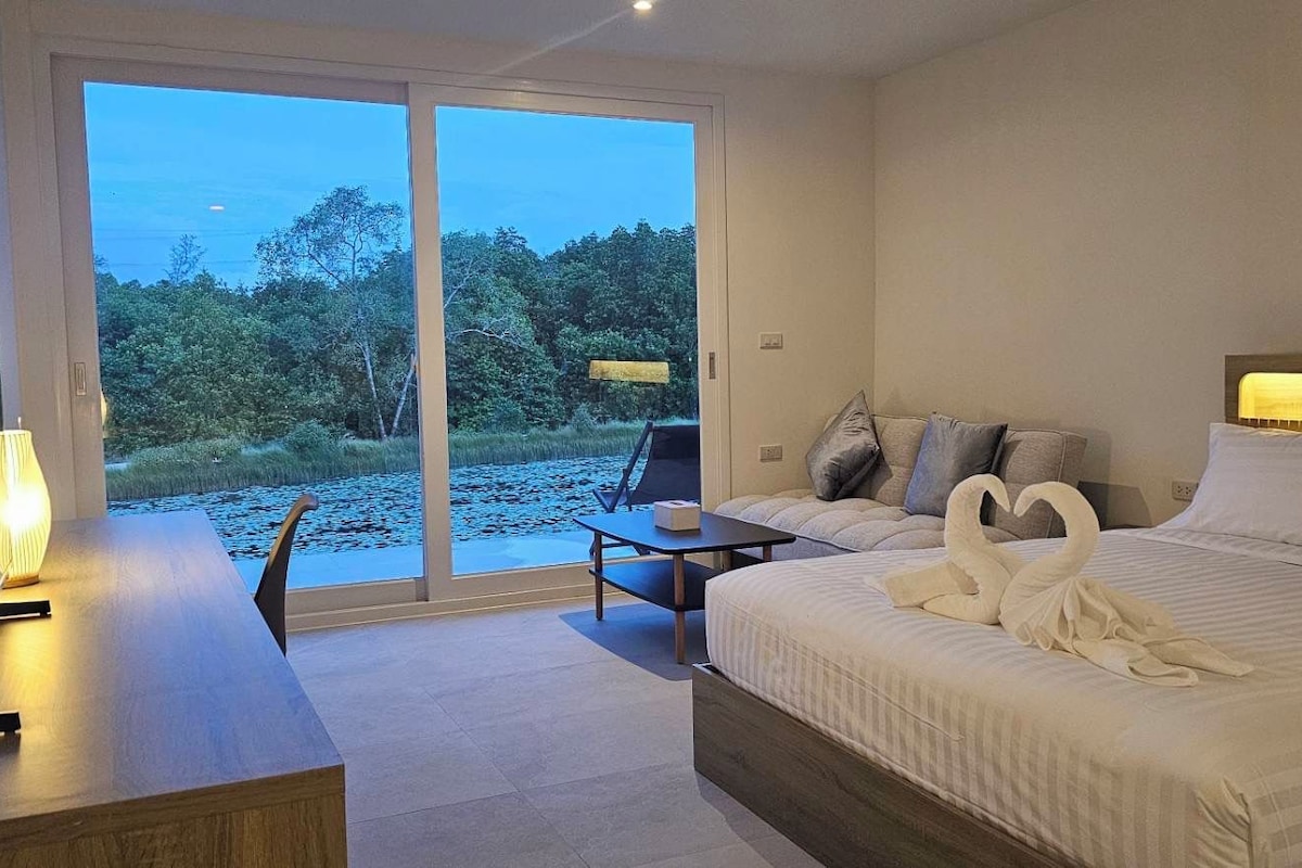 Ein Hotelzimmer mit Bett, Schreibtisch, Stuhl und Blick auf eine natürliche Landschaft durch eine Schiebetür.