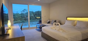 Ein Hotelzimmer mit Bett, Schreibtisch, Stuhl und Blick auf eine natürliche Landschaft durch eine Schiebetür.