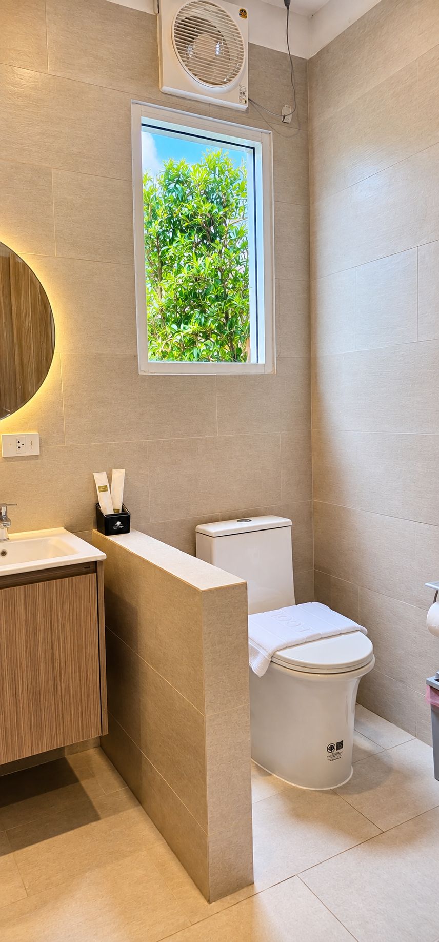 Ein modernes Badezimmer mit Toilette, Waschbecken und einem Fenster mit Blick auf Grünflächen.