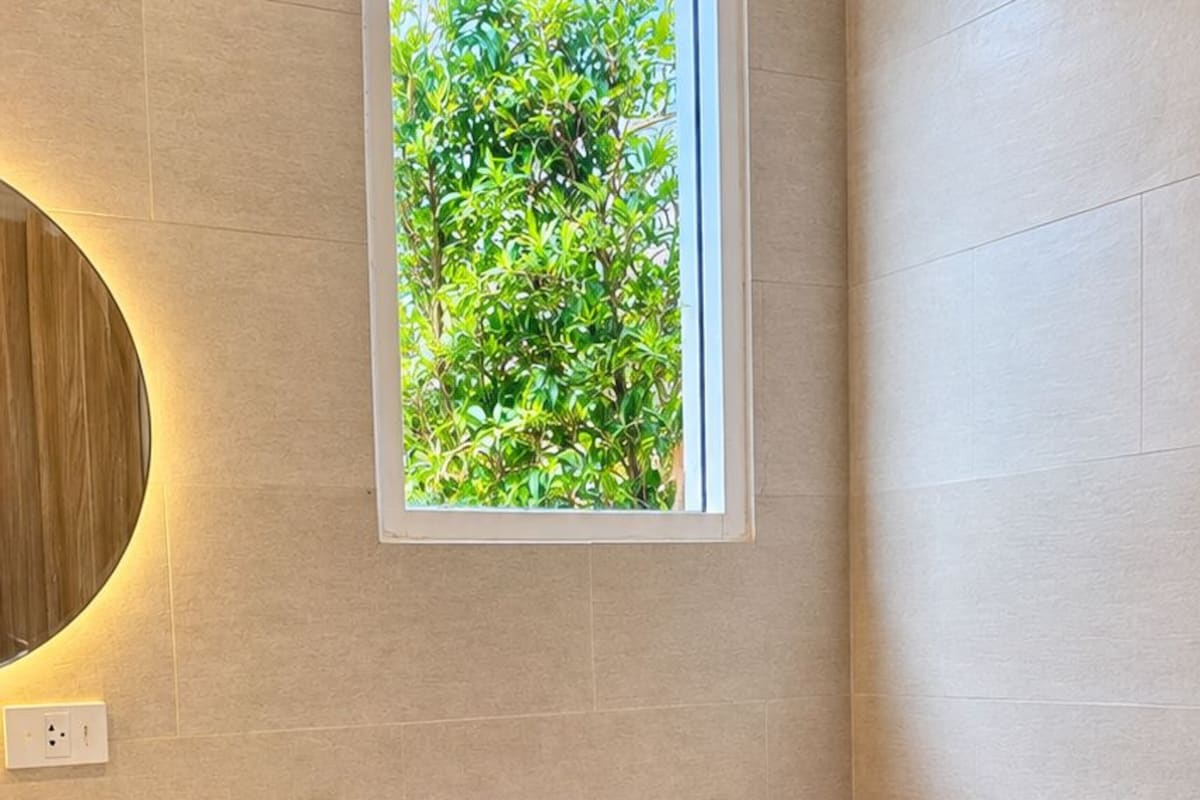 A modern bathroom with a toilet, sink, and a window with a view of greenery.