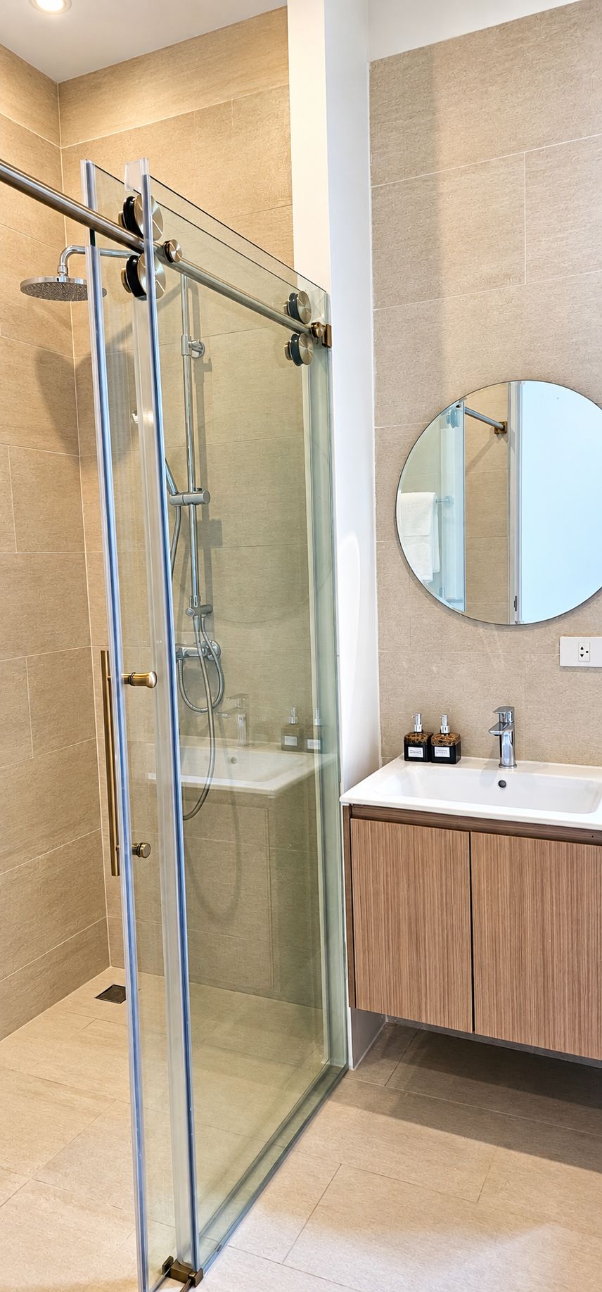 Un baño moderno con ducha envuelta en vidrio, un espejo redondo y armarios de madera.