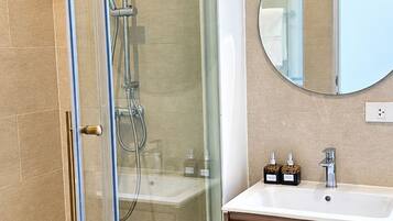 Un baño moderno con ducha envuelta en vidrio, un espejo redondo y armarios de madera.