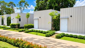 A row of modern, single-story buildings with white doors and windows, surrounded by well-maintained landscaping and trees. - Mangrove Resort Phuket Airport (Thalang)