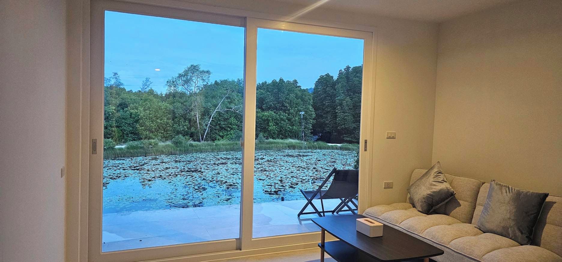 A room with a sliding glass door leading to a pond, a sofa, and a small table.