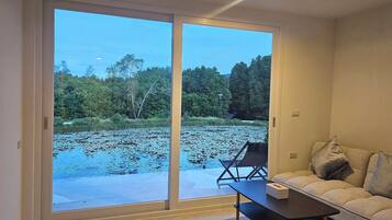 A room with a sliding glass door leading to a pond, a sofa, and a small table.