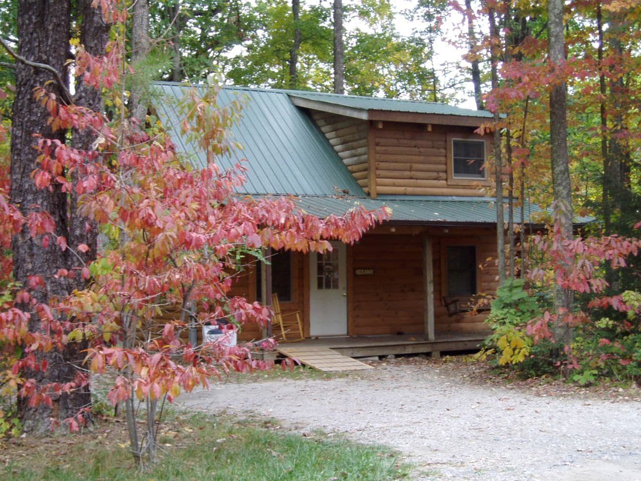 A log cabin with a porch, surrounded by trees with autumn foliage.