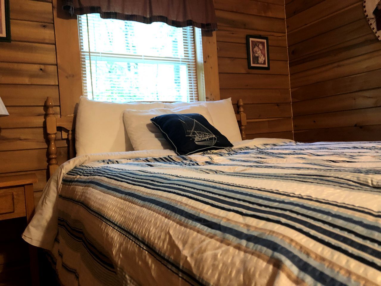 A wooden cabin-style bedroom with a bed, a window with blinds, and a picture on the wall.