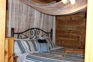 A wooden cabin room with a bed, curtains, and a hanging light fixture. - Rustic Cabin Rental in the Forest near Charleston, West Virginia (Hico)