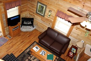 A cozy cabin interior with a leather sofa, a television, and a fireplace. - Rustic Cabin Rental in the Forest near Charleston, West Virginia (Hico)