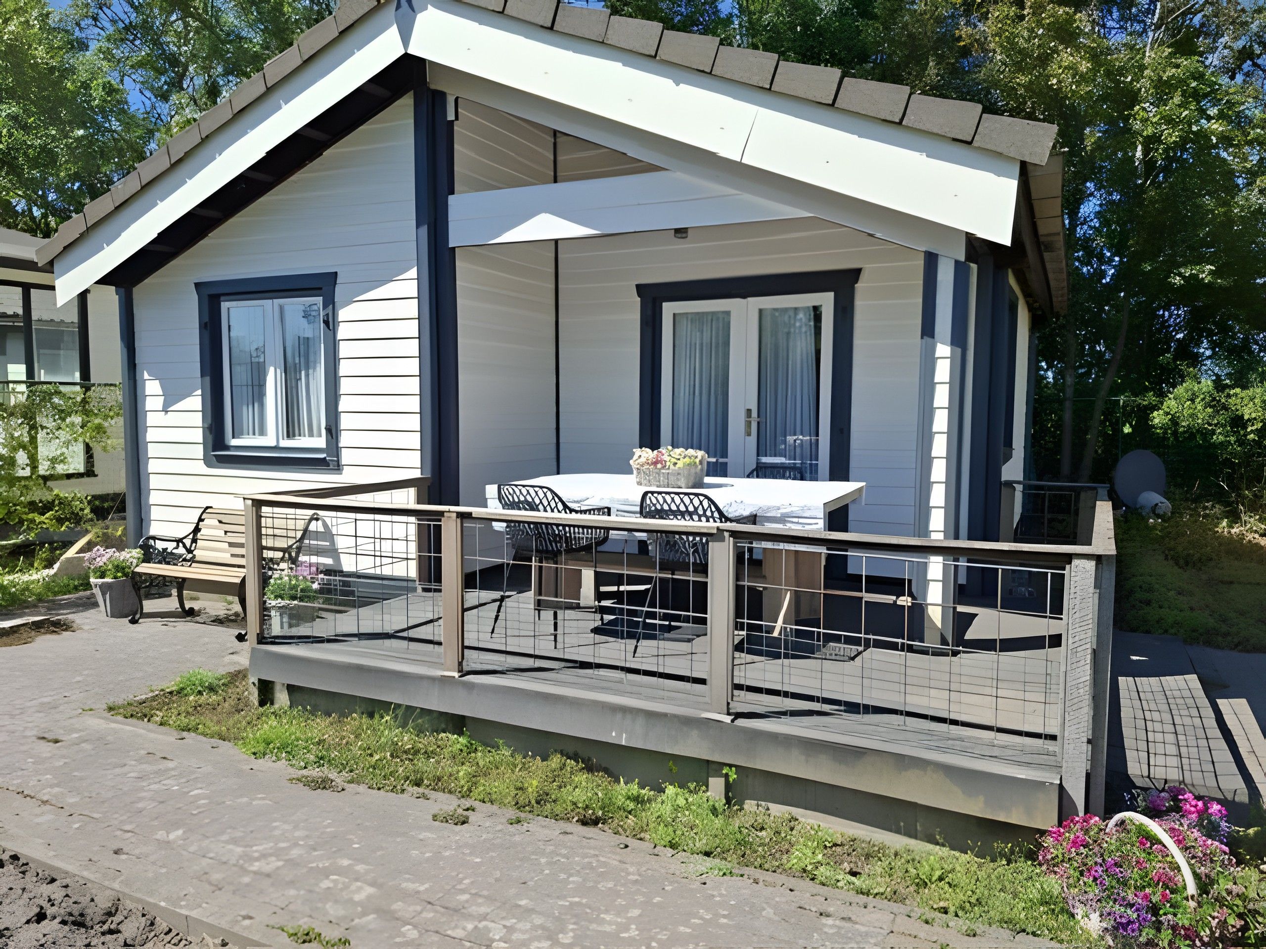 A single-story cabin with a balcony, a dining table with chairs, and a small garden area.