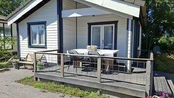 A single-story cabin with a balcony, a dining table with chairs, and a small garden area.
