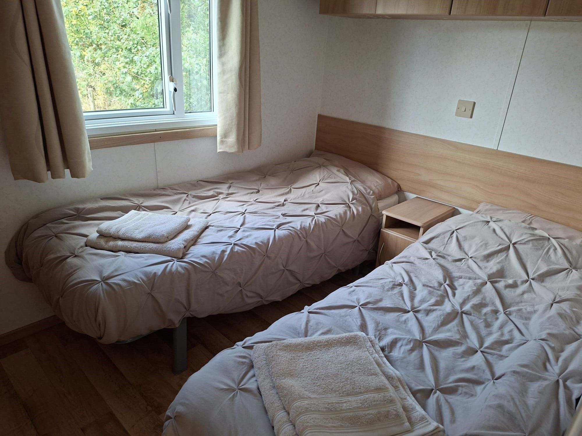 A bedroom with two beds, a window with curtains, and a wooden headboard.