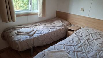 A bedroom with two beds, a window with curtains, and a wooden headboard.
